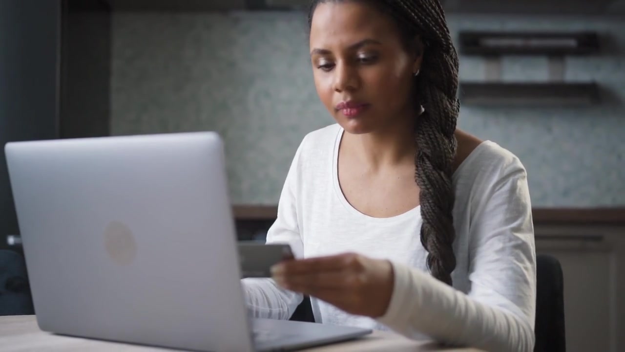 A woman holding a payment card while using her laptop